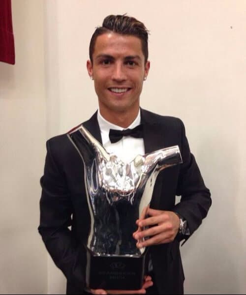 A man smiling and holding a trophy with his half up half down hairstyle