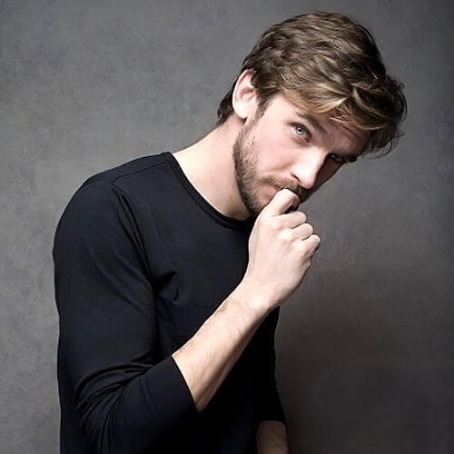 A man touching his chin with his Dan Stevens layered hairstyle