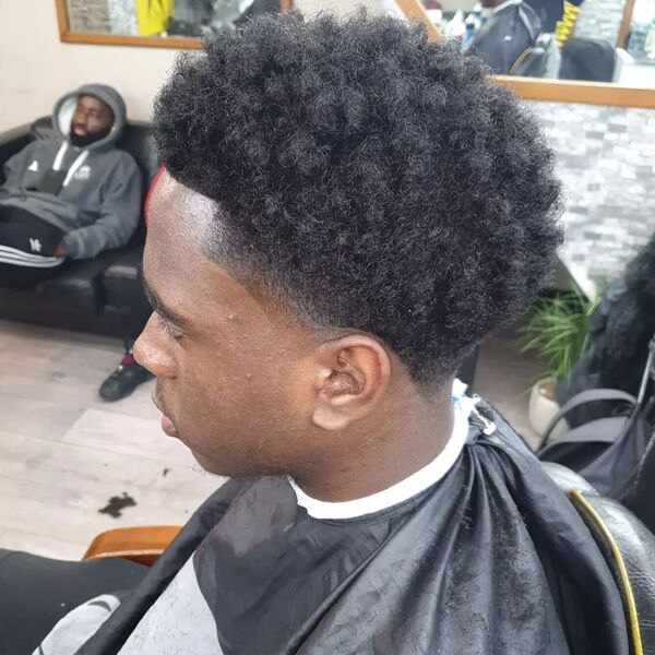Afro Curls with Taper Fade- a man wearing a black barber's cape