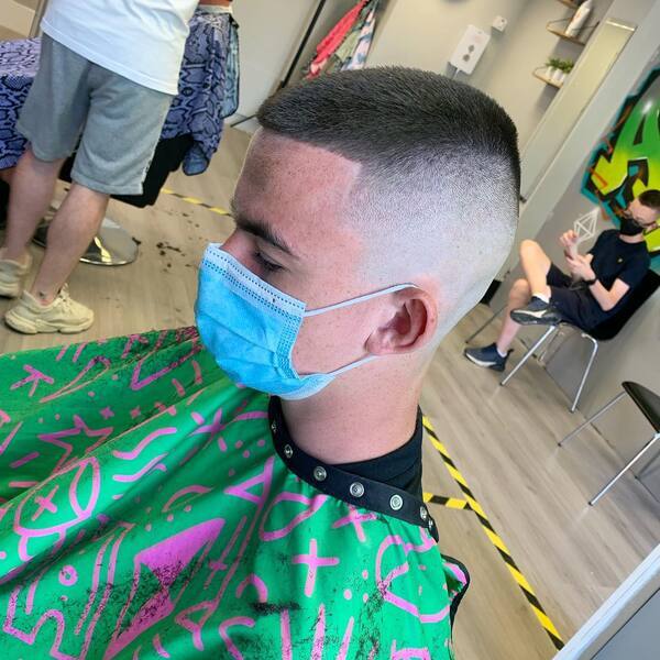 Barber's Buzz Cut- a man wearing a blue face mask and green barber's cape Baseball Haircuts