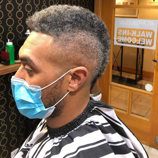 Faux Hawk Fade with Thick Curls- a man wearing a blue face mask and a barber's cape