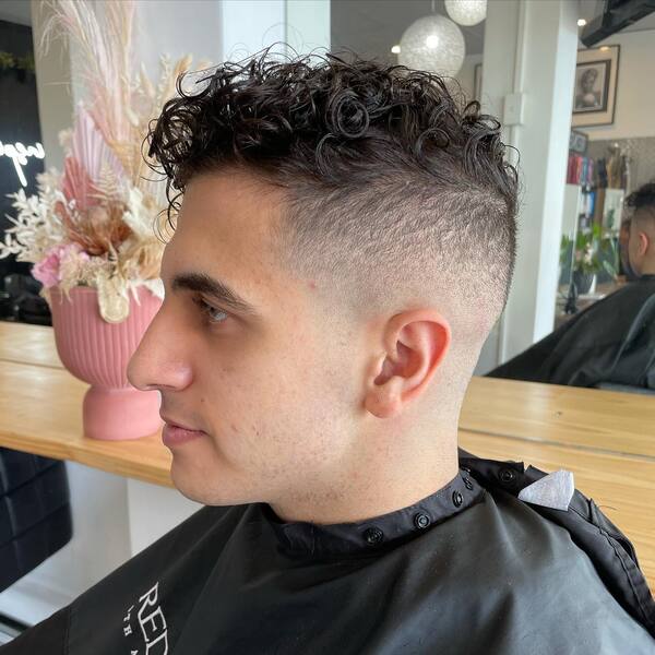 Messy Curly Top with Skin Fade- a man wearing a black barber's cape Baseball Haircuts