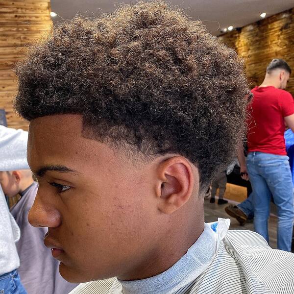 Thick Messy Afro Curls with Taper Fade- a man wearing a white barber's cape